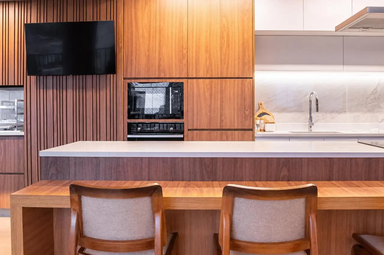 Cozinha contemporânea com bancada clara, marcenaria em madeira e frontão em pedra